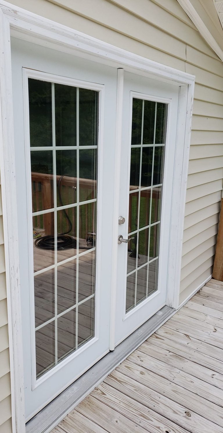 White French doors with multi-pane glass panels on a wooden deck attached to a beige vinyl-sided house
